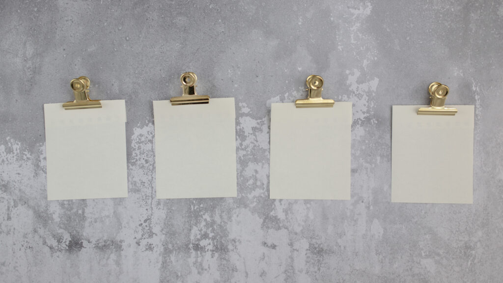 Blank stickers for notes attached with gold holders and hung on gray wall