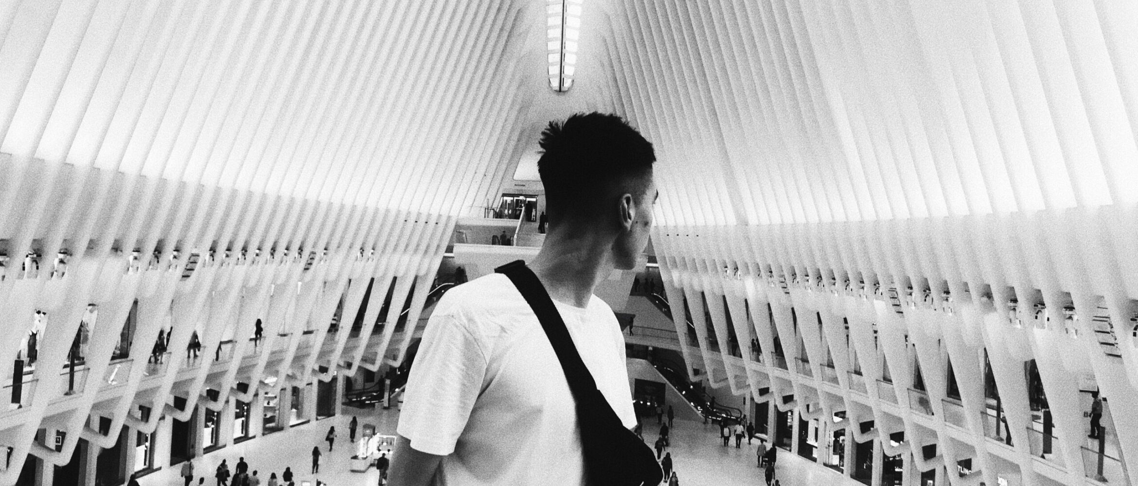 Black and white of young guy with waist bag admiring geometric ceiling of contemporary building