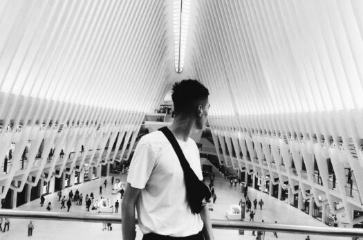Black and white of young guy with waist bag admiring geometric ceiling of contemporary building