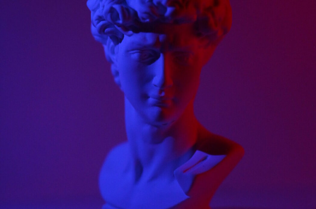 Bust of young male on plinth placed on white surface in dark studio in blue and red lights