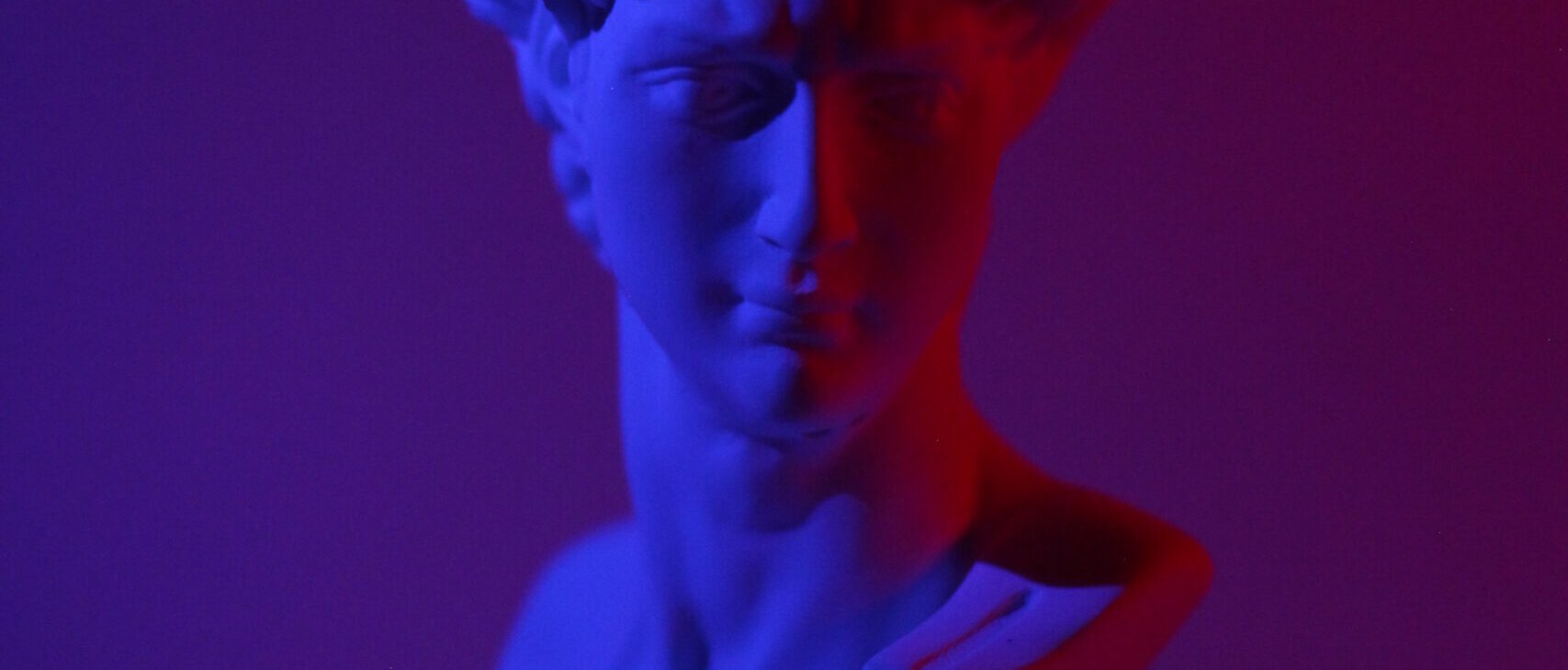 Bust of young male on plinth placed on white surface in dark studio in blue and red lights