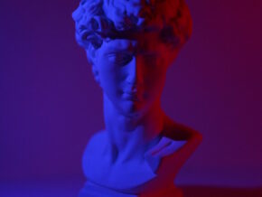 Bust of young male on plinth placed on white surface in dark studio in blue and red lights