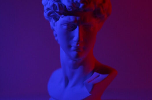 Bust of young male on plinth placed on white surface in dark studio in blue and red lights