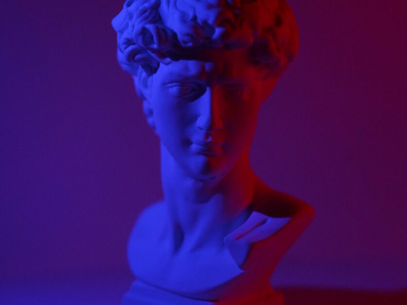 Bust of young male on plinth placed on white surface in dark studio in blue and red lights