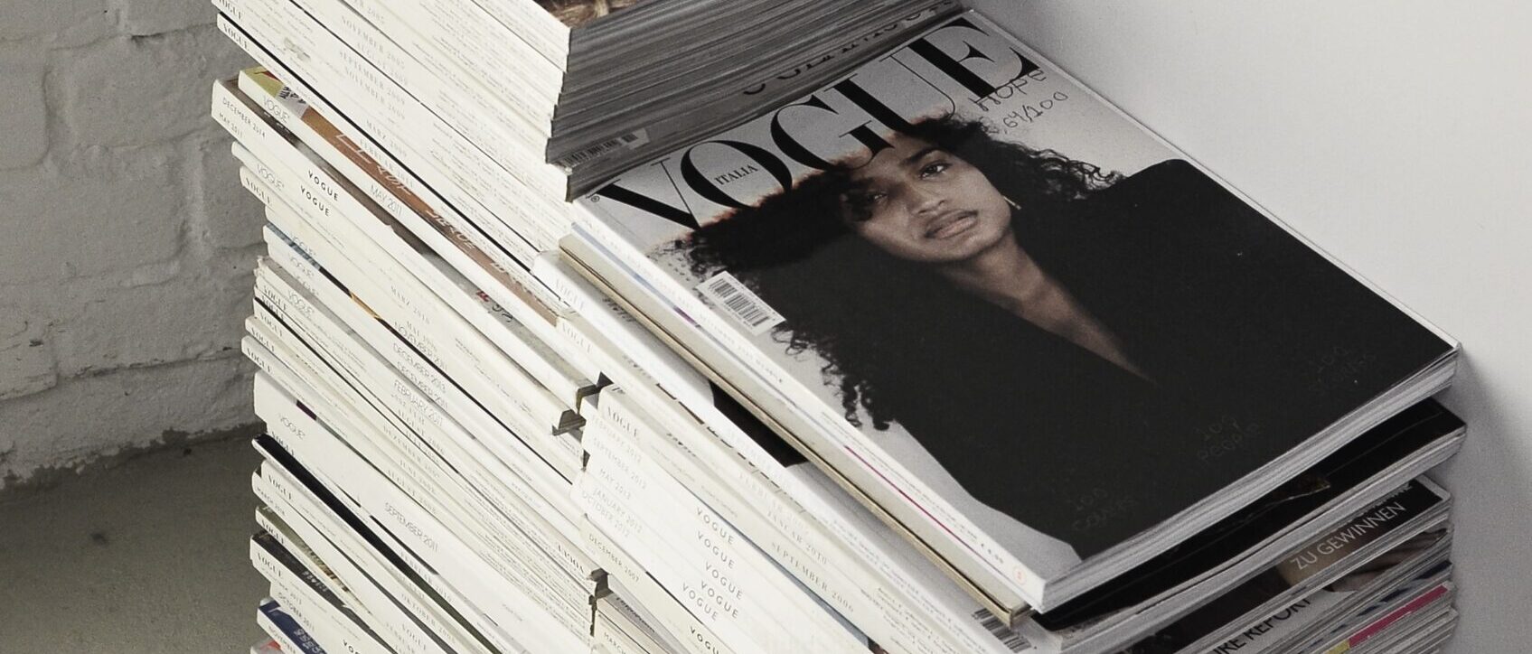 High angle many fashion magazines stacked on floor against white brick wall in studio