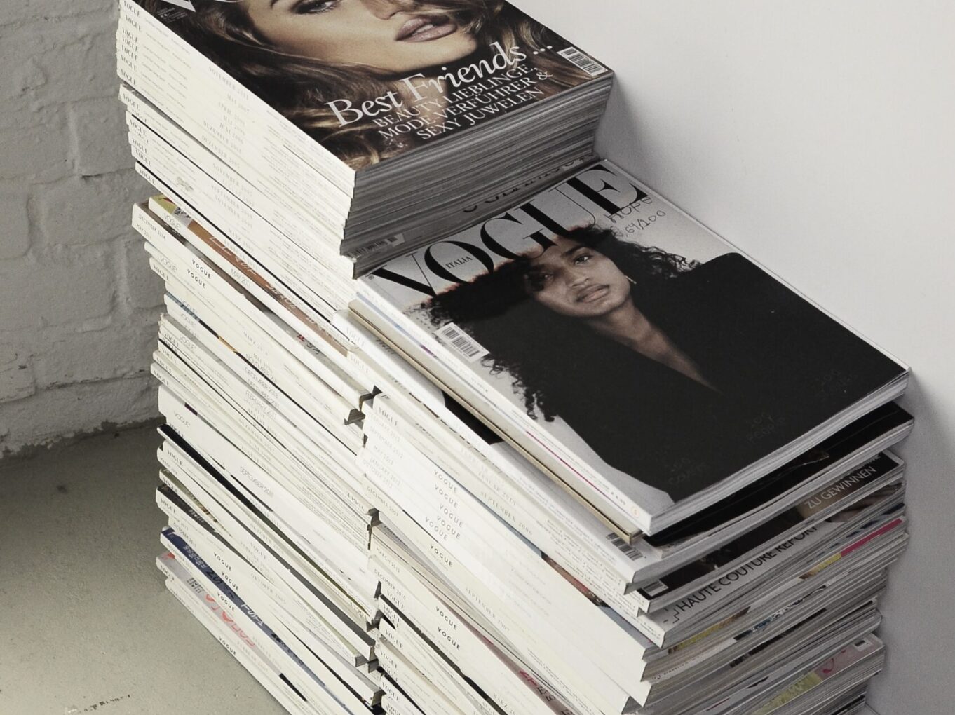 High angle many fashion magazines stacked on floor against white brick wall in studio