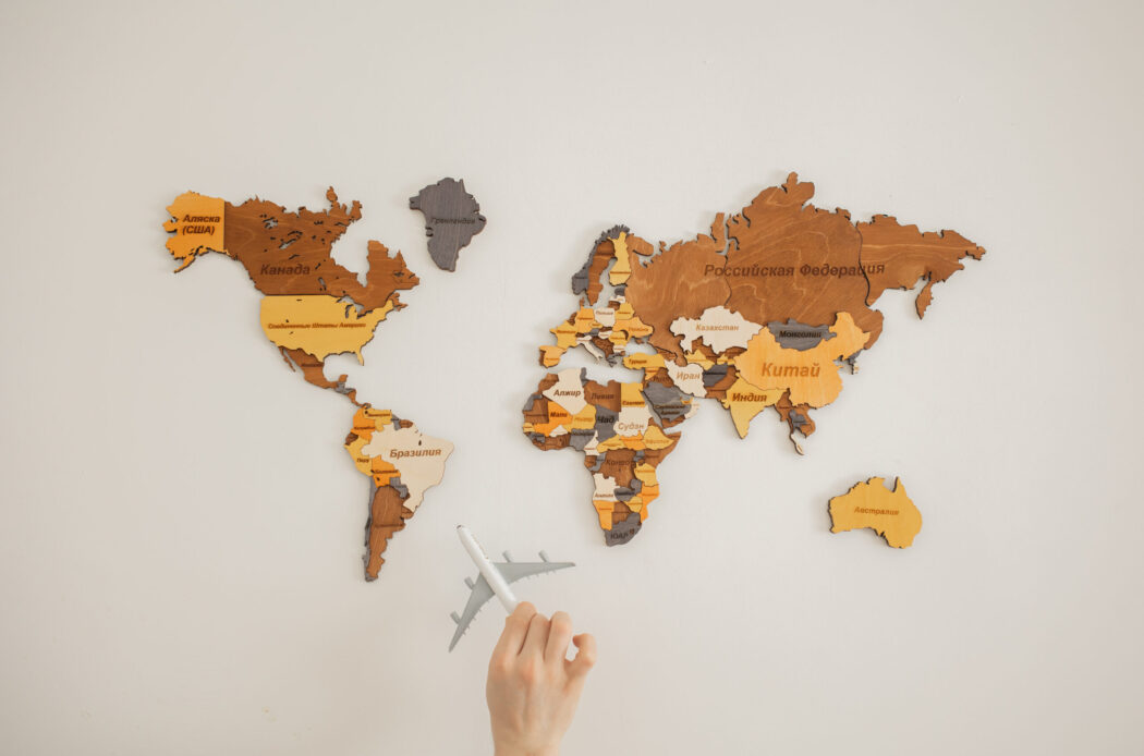 Crop unrecognizable person with toy aircraft near multicolored decorative world map with continents attached on white background in light studio