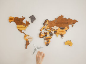 Crop unrecognizable person with toy aircraft near multicolored decorative world map with continents attached on white background in light studio