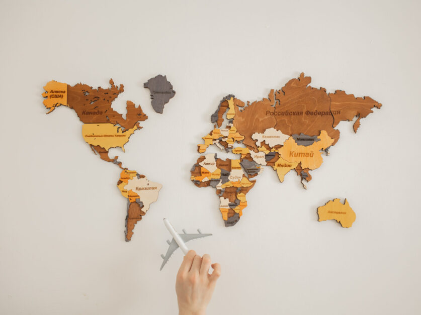 Crop unrecognizable person with toy aircraft near multicolored decorative world map with continents attached on white background in light studio